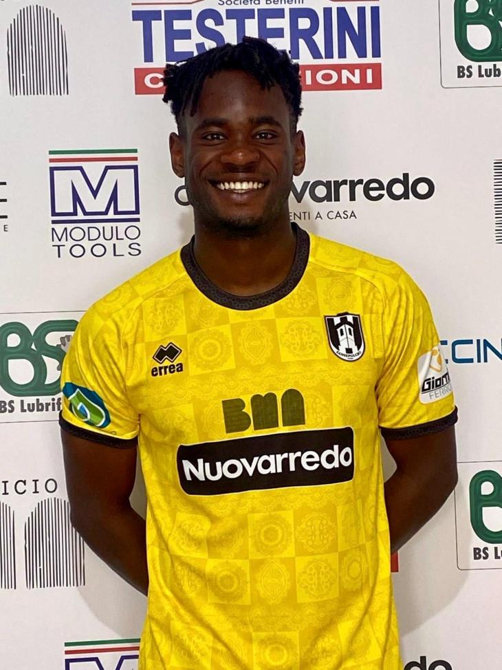 Giocatore sorridente indossa una maglia gialla con dettagli neri, posa davanti a uno sfondo con loghi e scritte.